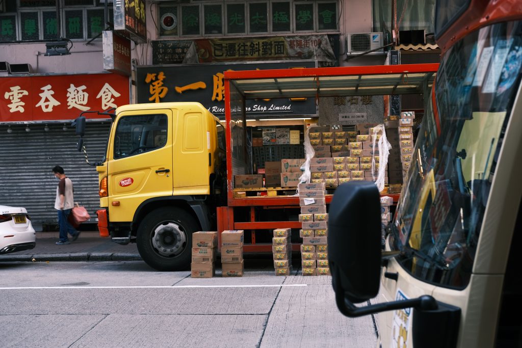 A yellow delivery truck unloading boxes in a bustling urban street market.